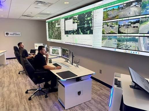 Two analysts at their desks in a Flock Safety real-time crime center, with FlockOS maps and live camera feeds across a large video wall