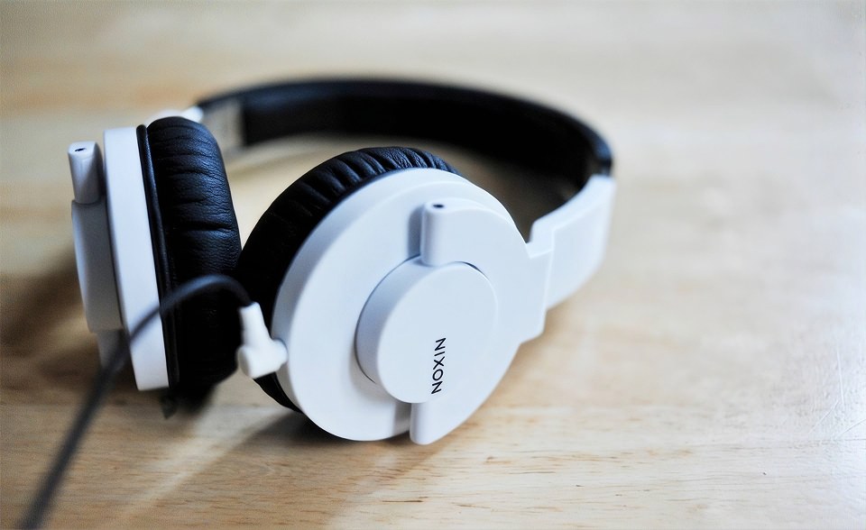 White Nixon Stylus headphones with black ear cushions resting on a light wooden table
