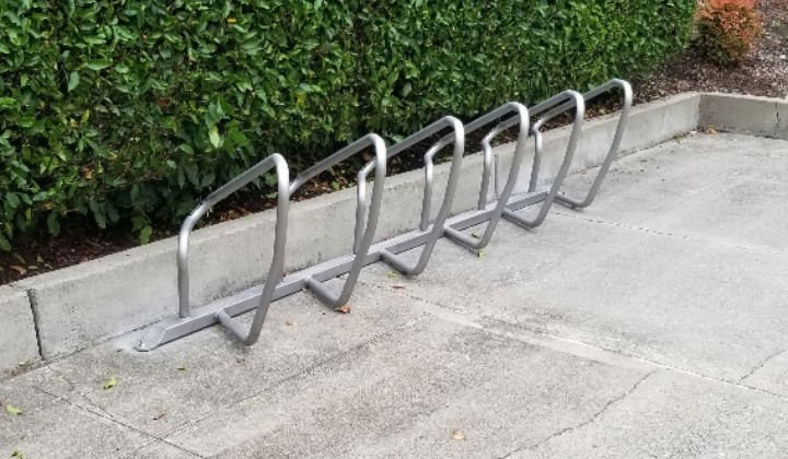 Plaza bike rack with five steel loops installed along a curb in front of a hedge