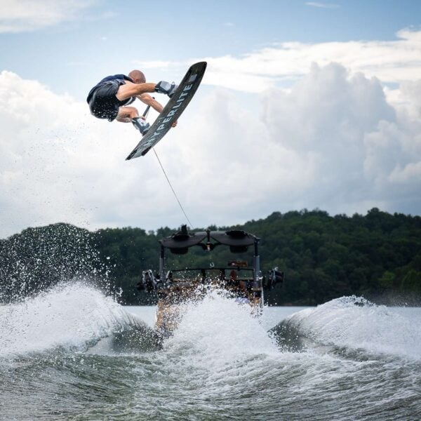 Rider mid-air on a Hyperlite wakeboard behind a boat, spray below